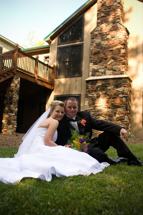 bride and groom sitting on grass in front of venue